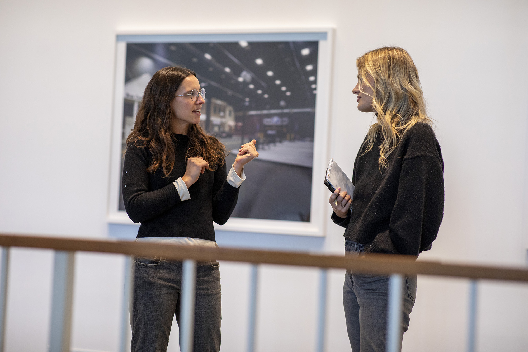 Two women standing and speaking in front of a framed photograph.